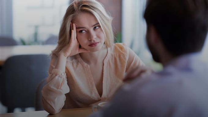 A disengaged employee resting her head on her hand and looking away during a conversation with a colleague, illustrating quiet quitting and workplace detachment