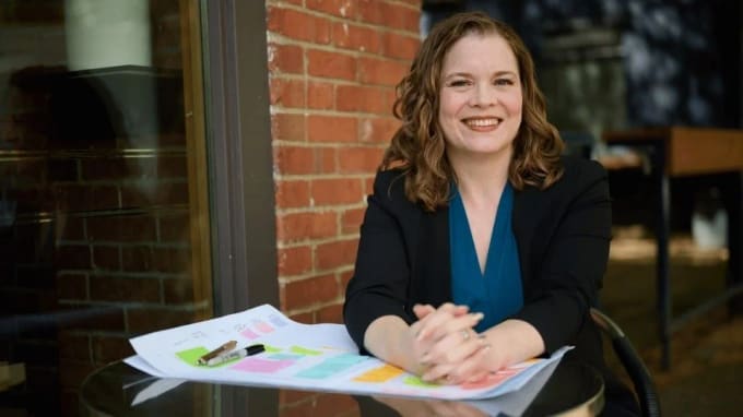 Sara Lobkovich, OKR coach and strategy consultant, smiling at an outdoor table with colorful strategic planning worksheets spread in front of her
