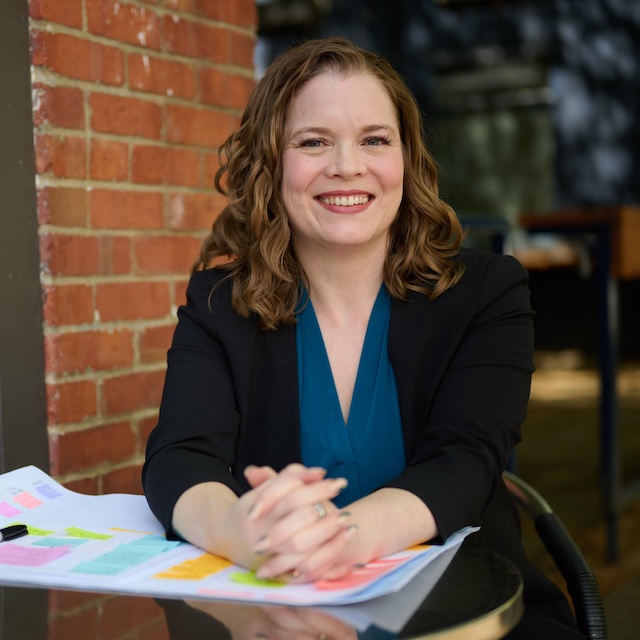 Sara Lobkovich at a cafe table with colorful sticky notes, wearing a black blazer and teal top